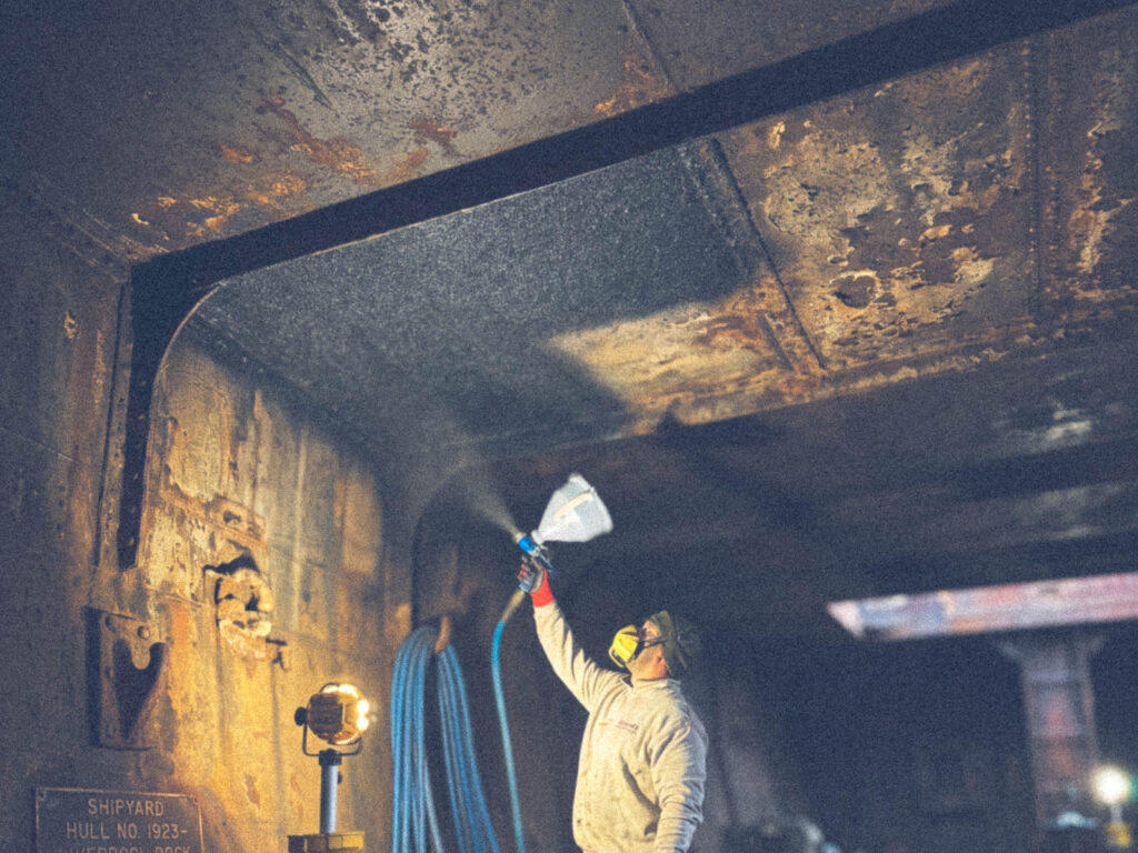 Applicator spraying a coating onto the barge overhead panels
