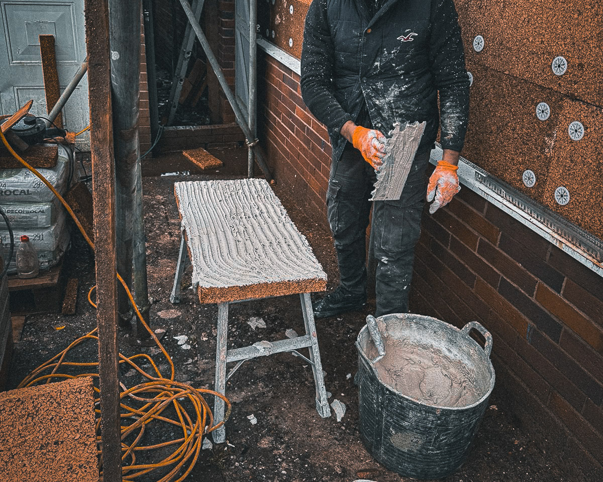 Applicator preparing adhesive on a cork insulation board beside mechanically fixed exterior cork boards