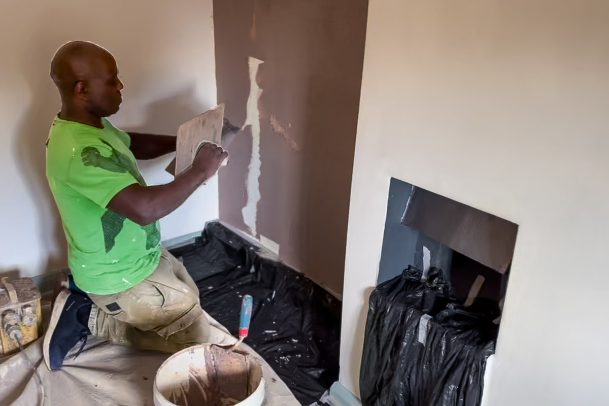 Applicator trowelling material onto an internal wall beside a fireplace