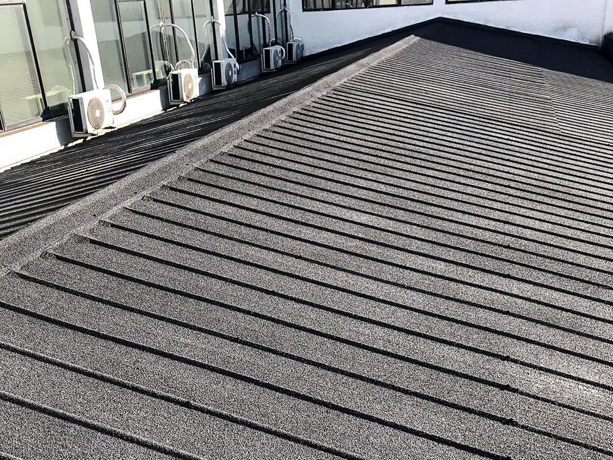 Textured grey coating on a profiled roof beside windows