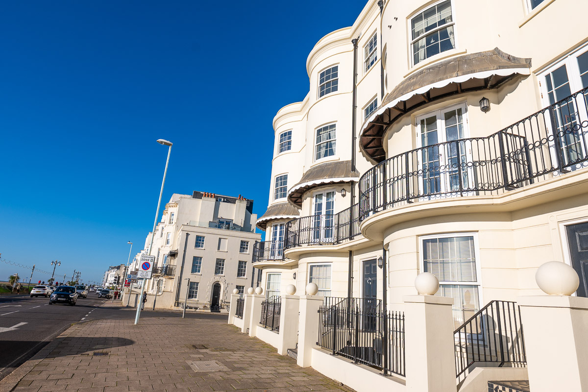 Cream-coloured coastal townhouses with curved balconies beside a seafront road