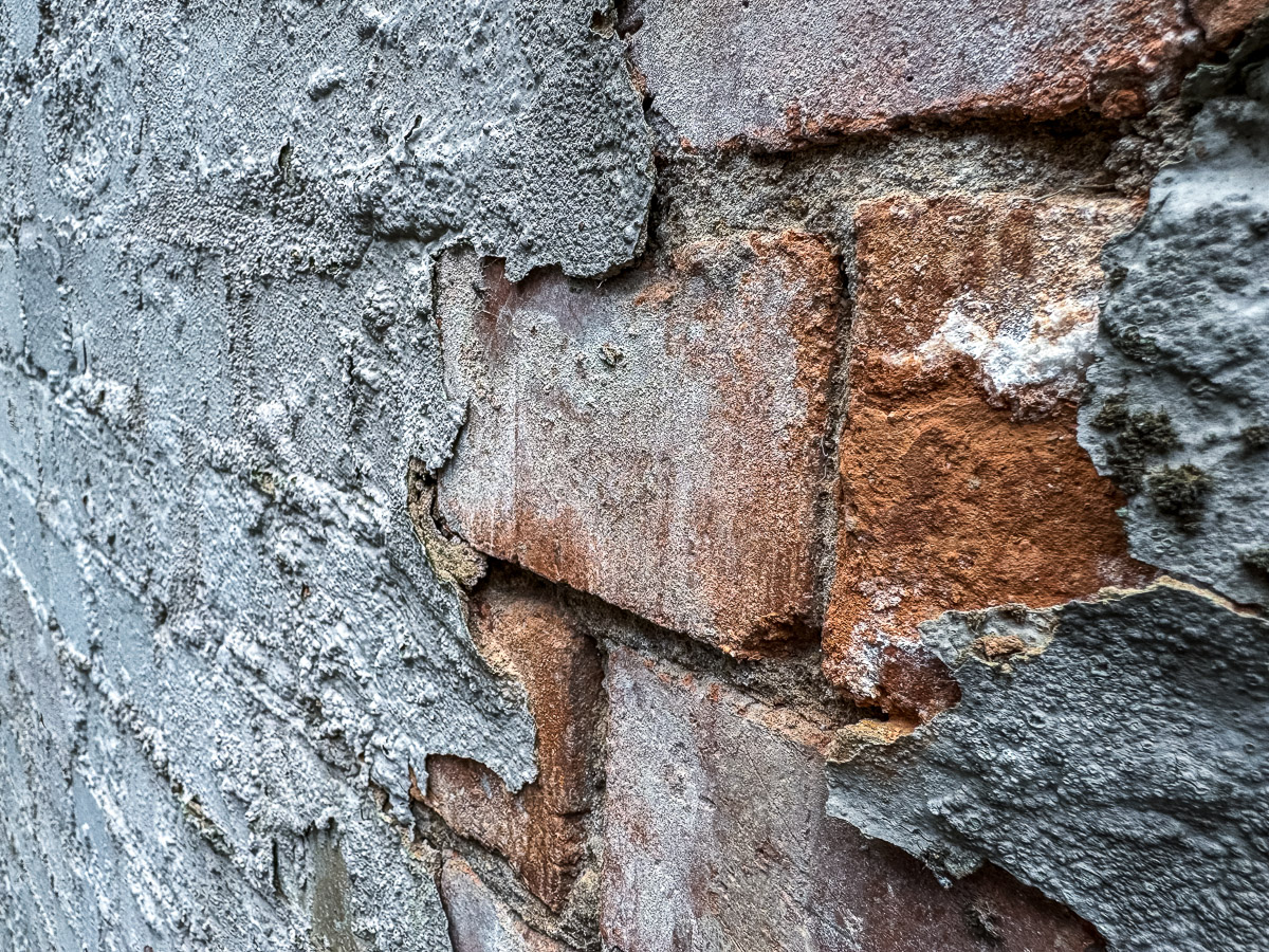 Damaged grey exterior render breaking away to expose red brickwork