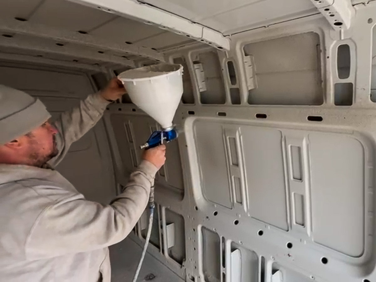 Applicator spraying cork coating onto the metal walls and ceiling inside a van