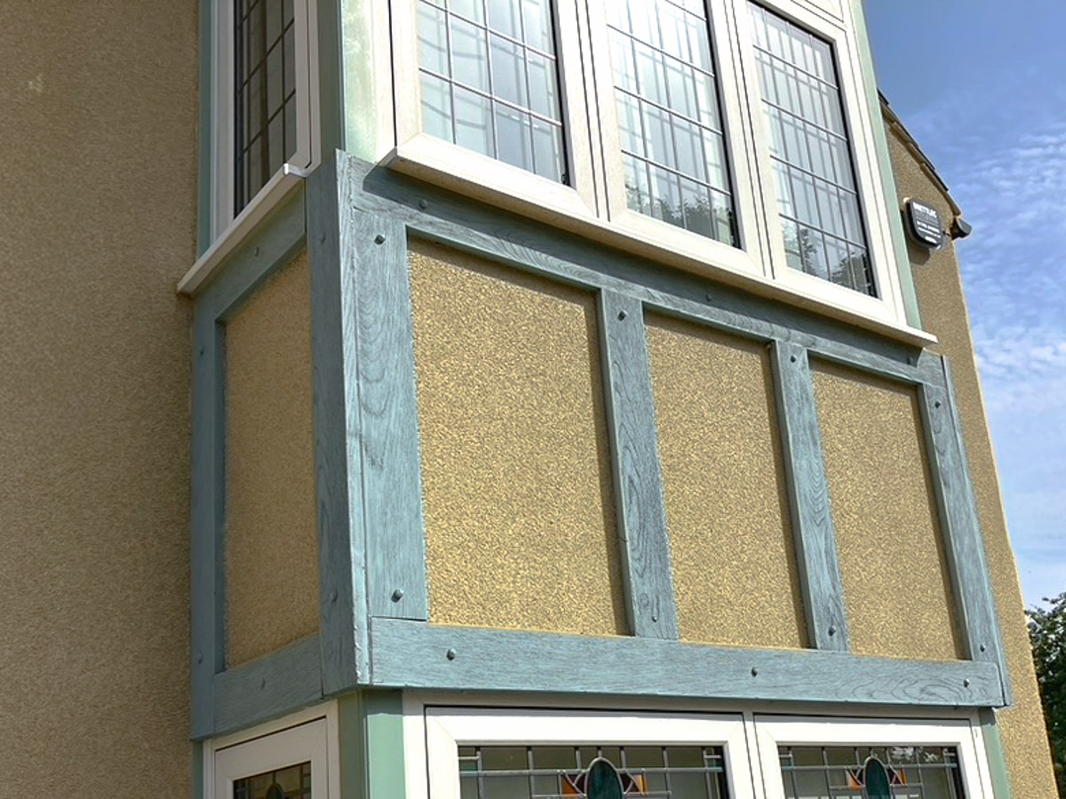 Rendered house façade with blue-grey timber detailing beneath a white bay window