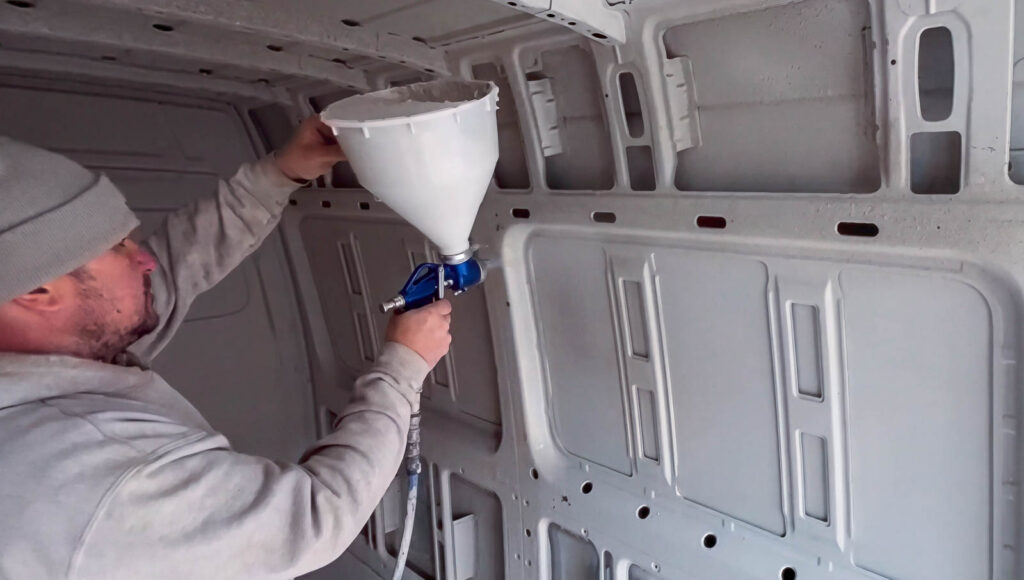 Spray gun applying cork coating around an interior van panel