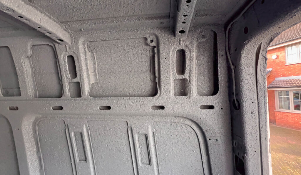 Textured spray-cork finish over a van wall, roof edge and structural rib
