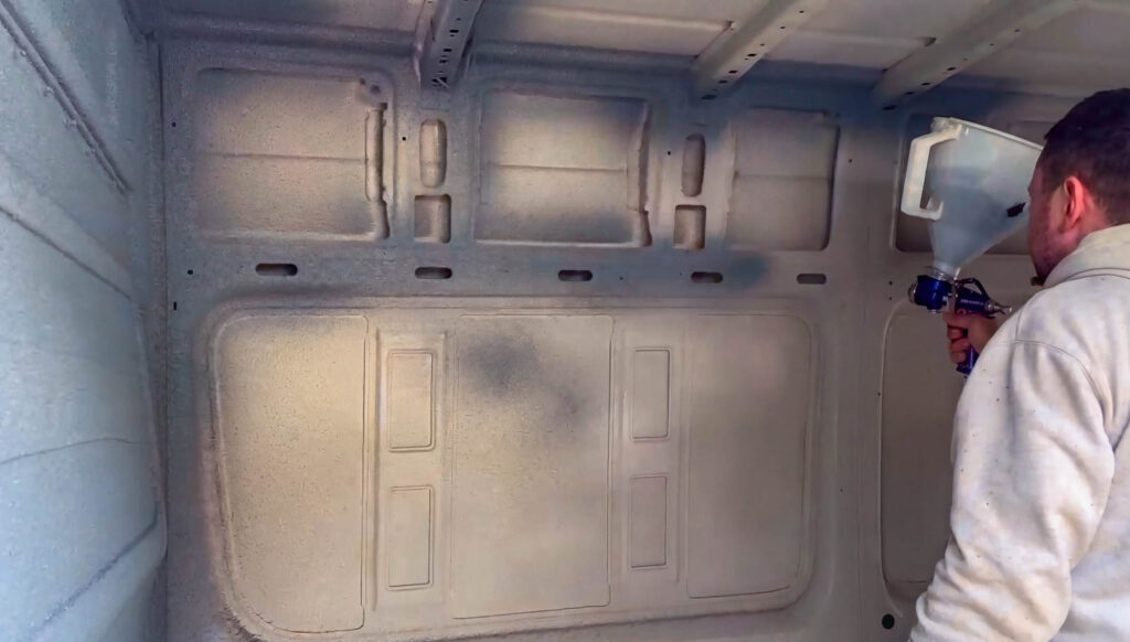 Installer spray-applying cork to the inside wall of a van