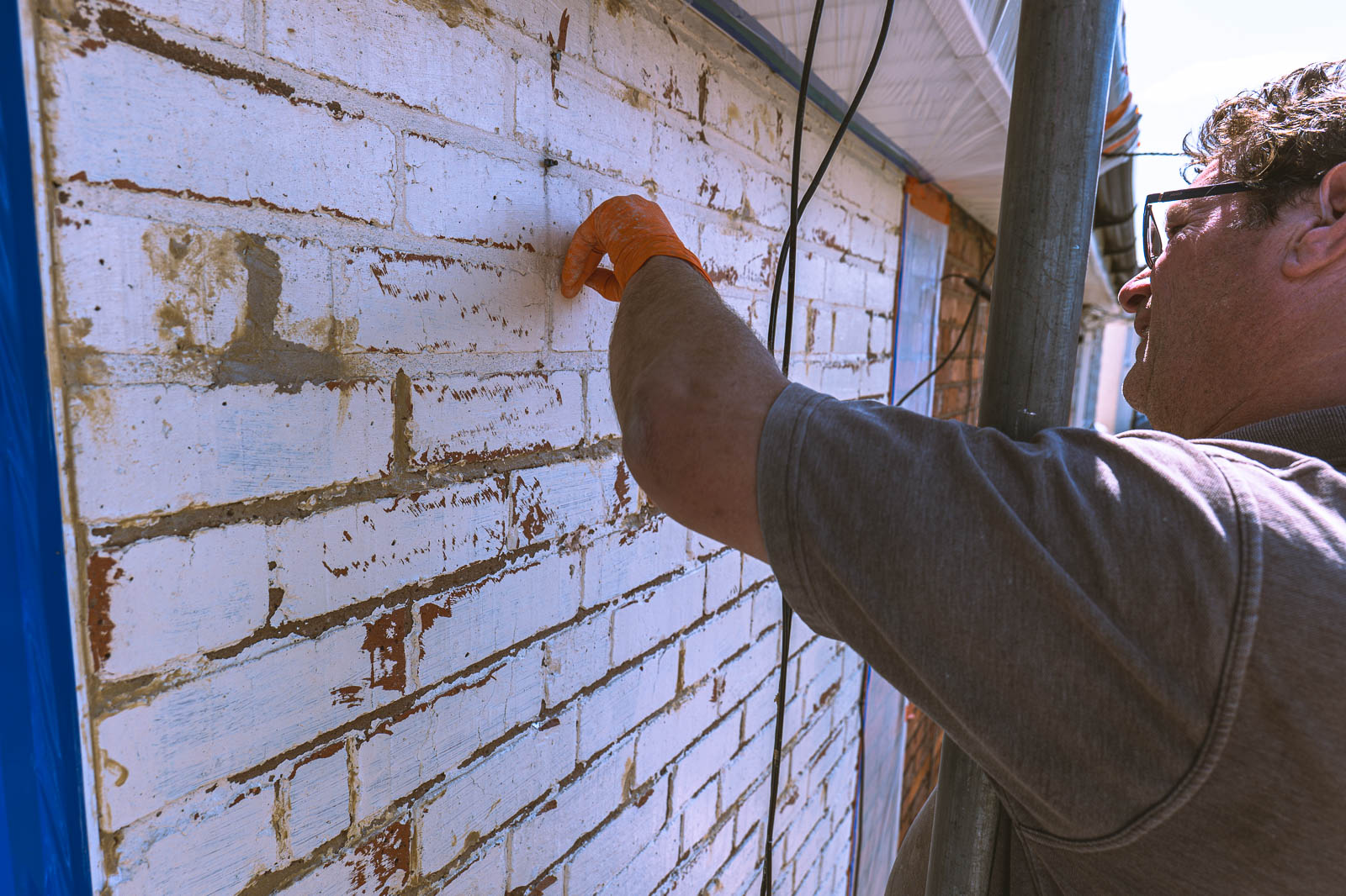 Applicator scraping loose material from painted Kings Norton masonry