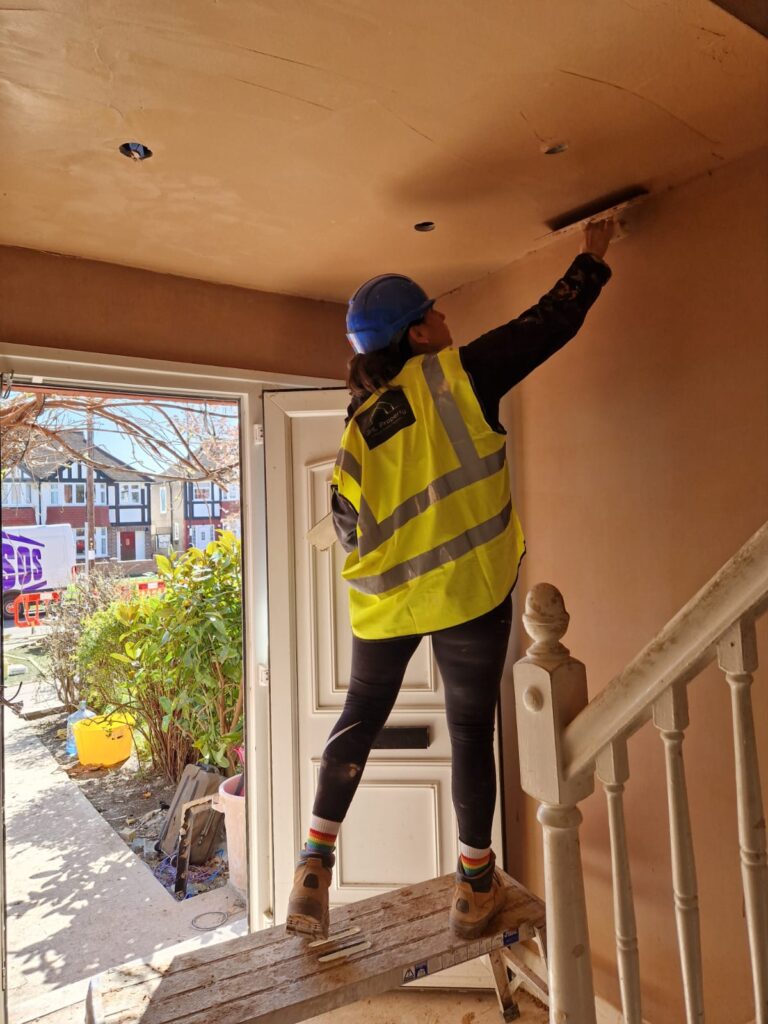 She Plasters applicator finishing an interior ceiling beside a staircase